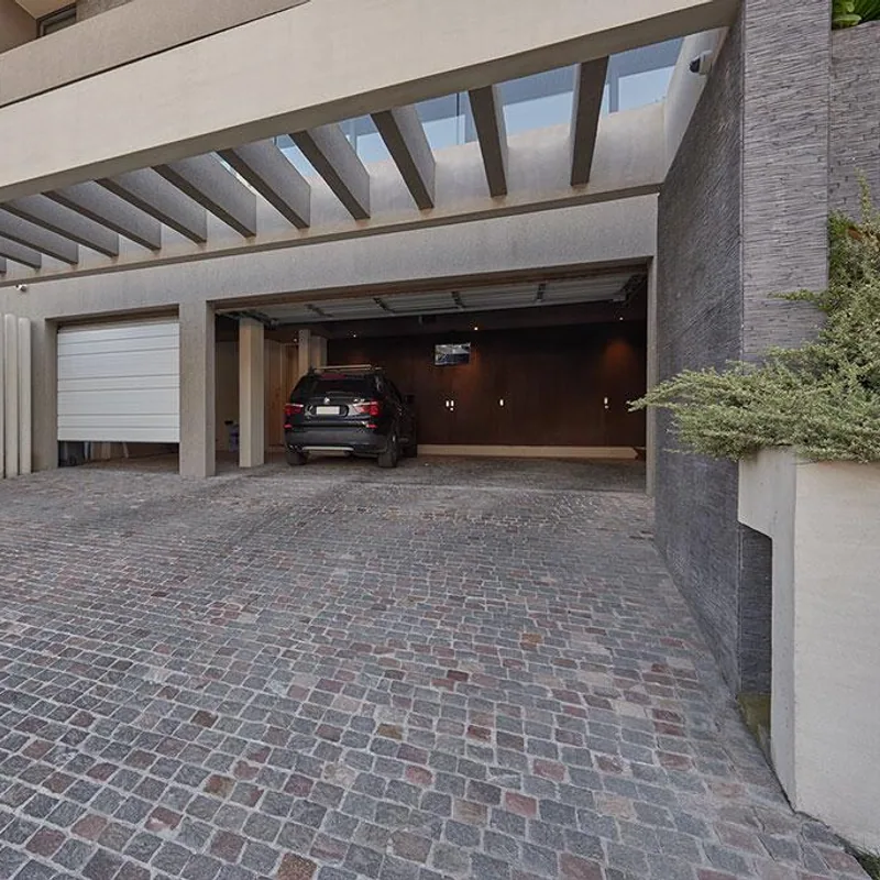 Acceso vehicular residencial con pavimento de piedra y garage iluminado